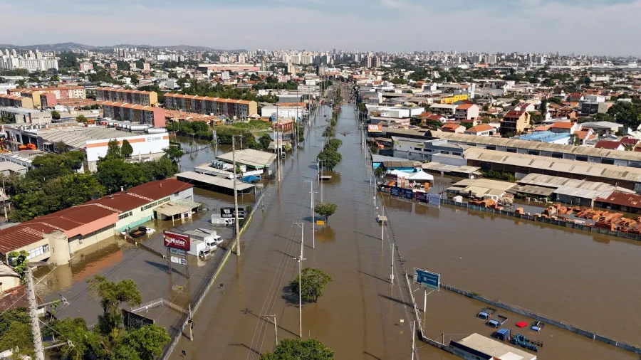 Rua alagada com moradores atravessando água contaminada após enchente