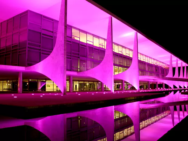 Fachada de prédio público iluminada com luz colorida durante campanha de saúde à noite